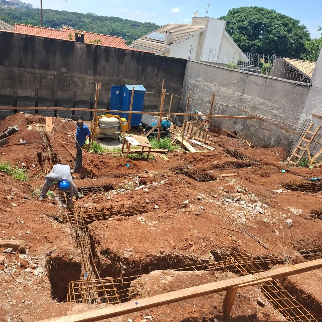 Trabalhadores posicionam armaduras de aço em valas abertas para a fundação da obra.
